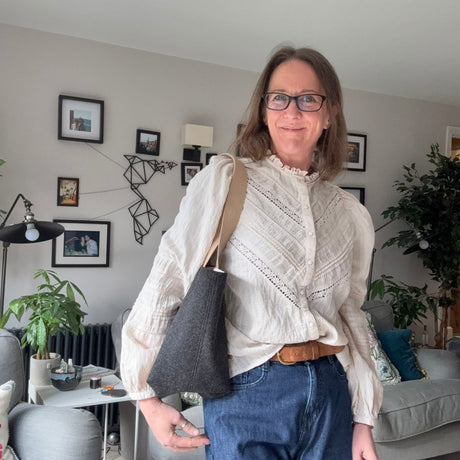 A woman wearing a white top and blue jeans is holding a gray tote bag with a flat, solid pattern.