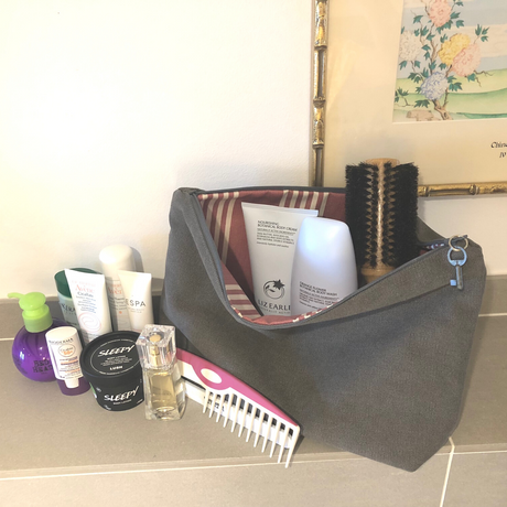 A large beige waterproof zipped toiletry bag with various items such as bottles, a brush, and a key pull laid out next to it, indicating its multifunctional use.