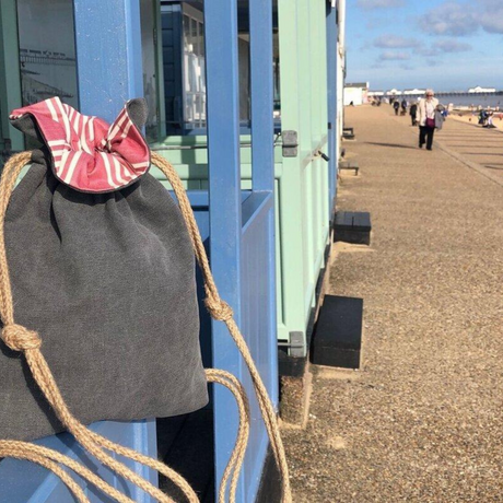 A gray drawstring backpack with a red and white striped drawstring closure, displayed on a bench near a beach setting.